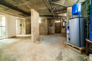 A large, empty room with a blue water tank in the corner. The room is bare and unoccupied